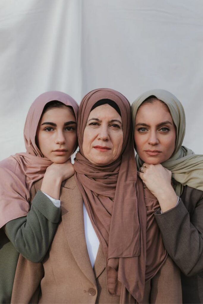 Three women in hijabs standing closely, showing unity and strength against a neutral background.