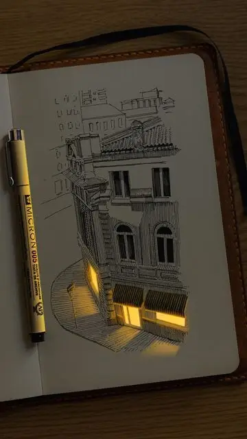 Sketch of a vintage building with glowing windows on a notebook, accompanied by a pen, creating a creative ambiance.