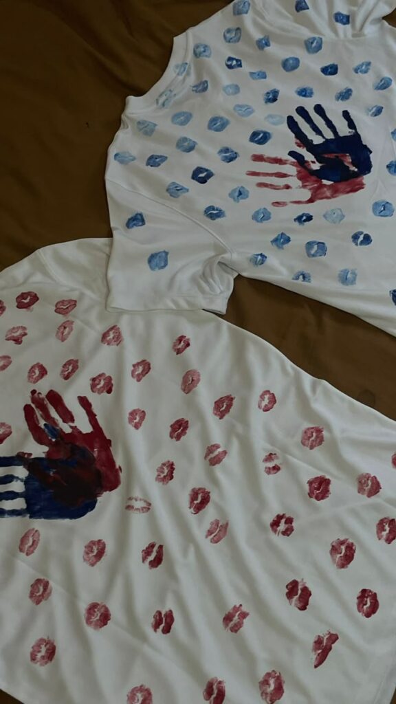 Hand-painted white t-shirts with red and blue handprints and dots, showcasing creative DIY designs on fabric.