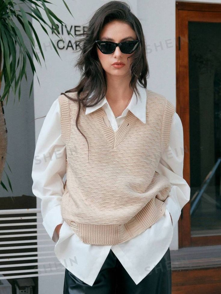 Woman in sunglasses wearing a beige sweater vest and white shirt, standing stylishly outdoors.