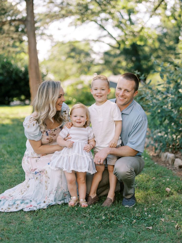 A happy family of four enjoys a sunny day in the park, smiling and posing together on the lush green grass.