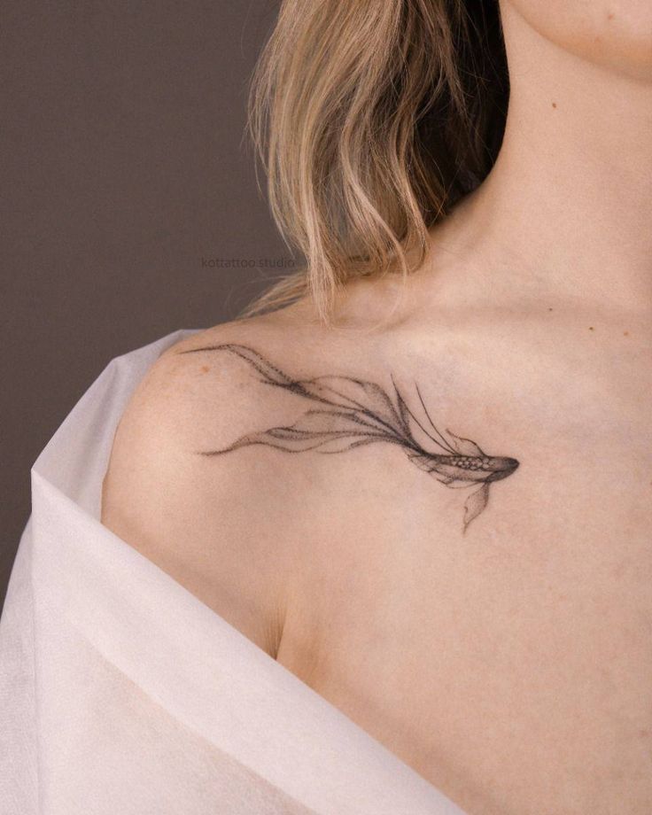 Delicate fish tattoo on shoulder, flowing design with fine lines, subtle and artistic.