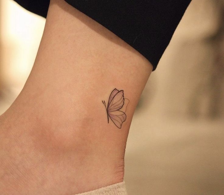 Minimalistic butterfly tattoo on ankle, close-up view with beige sock and black pants background.