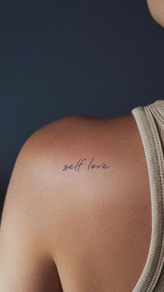 Shoulder tattoo of the words self love on a person's skin, emphasizing personal care and positive mental health.