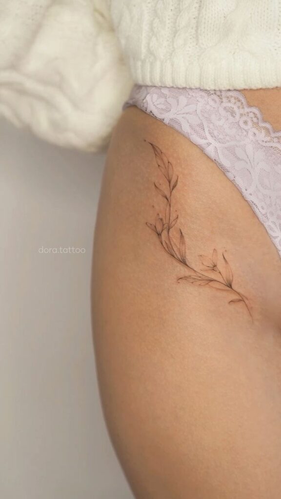 Minimalist floral thigh tattoo with lavender lace underwear and white sweater background.