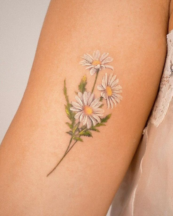 Delicate daisy tattoo on arm, featuring three flowers with green stems, showcasing a natural floral design.