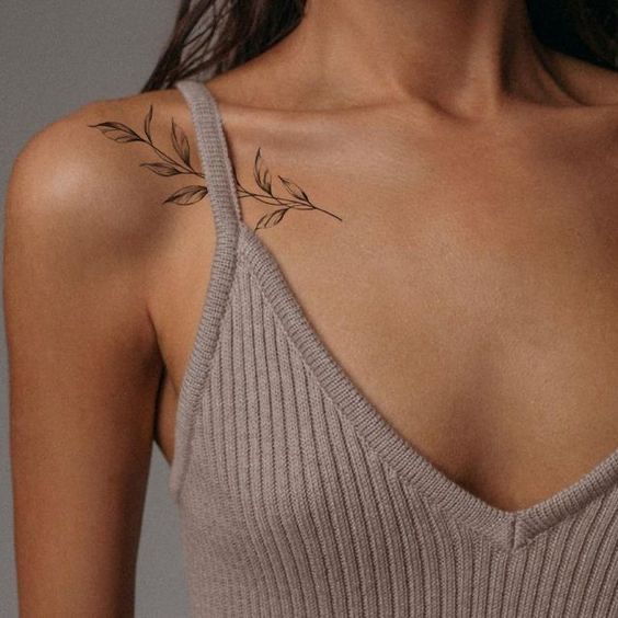 Woman wearing knit top with floral shoulder tattoo, showcasing delicate botanical art and fashion style.