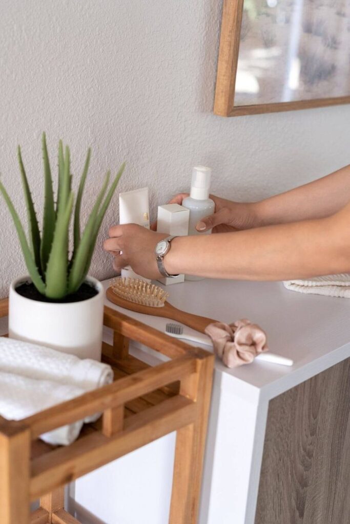 Person arranging beauty products on a bathroom counter with plant and wooden organizer.