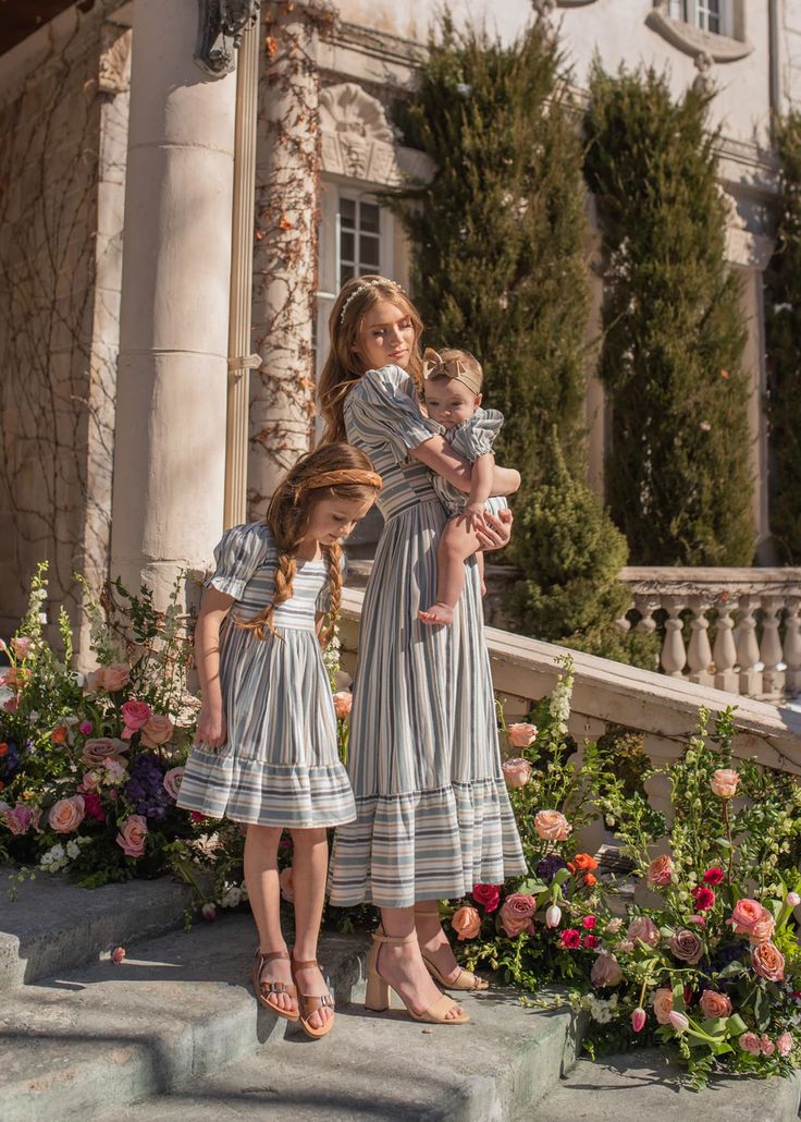 Family in matching striped dresses on stone steps surrounded by flowers, standing outside a classic building.