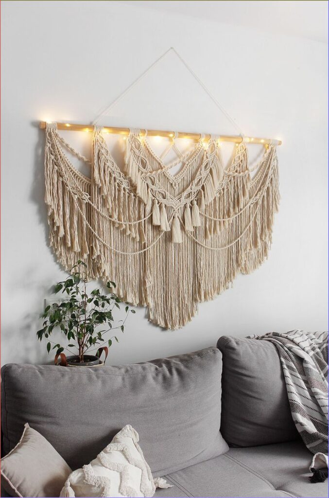 Cozy living room with a large macramé wall hanging, soft grey couch, and potted plant.