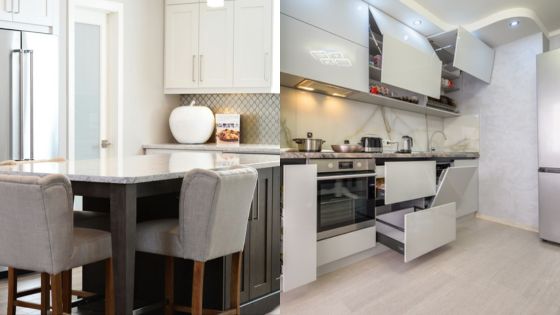 Modern kitchen interior with island, bar stools, and sleek cabinets, showcasing contemporary design and functionality.