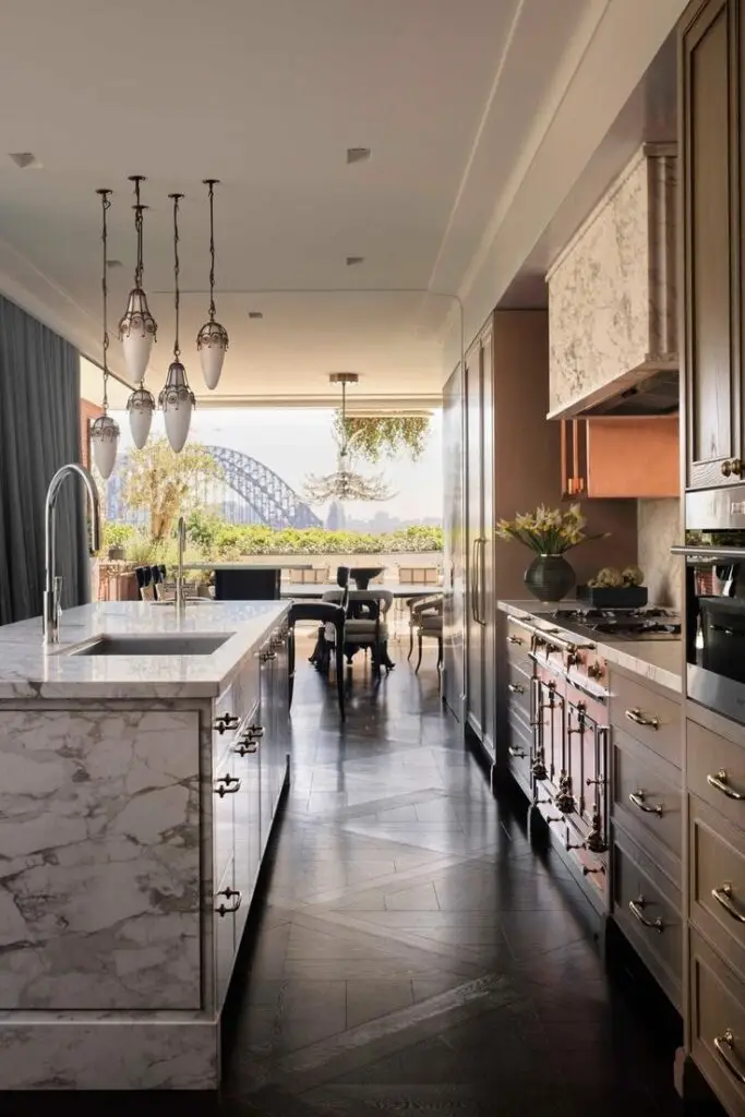 Luxurious modern kitchen with marble island, chic lighting, and expansive view of bridge and greenery.