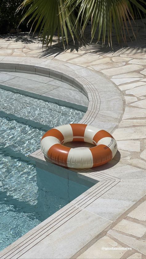 Orange and white pool float resting on the edge of a sunny swimming pool surrounded by palm leaves.