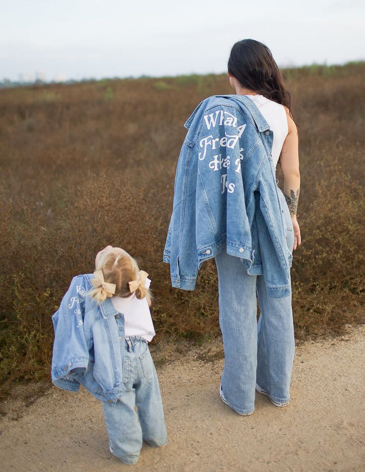 Mother and daughter in matching denim outfits walking on a dirt path in nature.