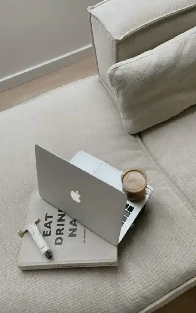 Laptop, book, and coffee on a cozy beige couch, creating a relaxing workspace vibe at home.