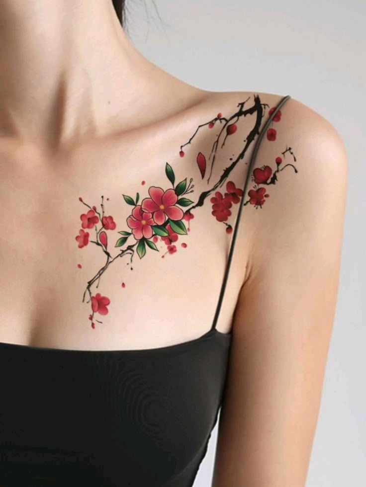 Floral shoulder tattoo with red blossoms and green leaves on a woman's skin, wearing a black camisole.