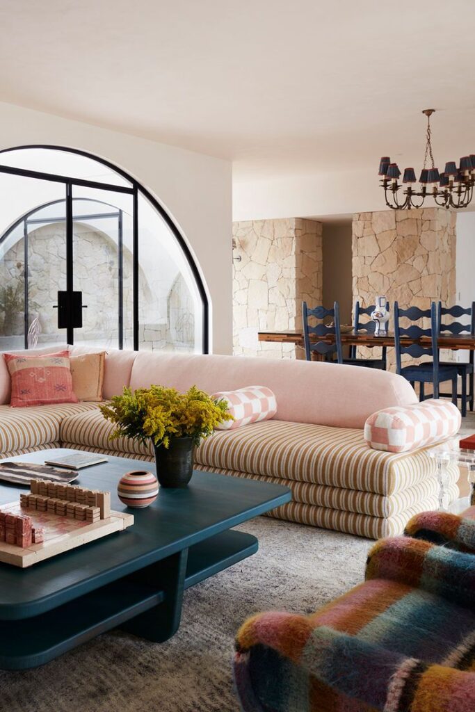 Stylish living room with striped sofa, blue coffee table, and stone walls. Bright, modern decor and arched window design.