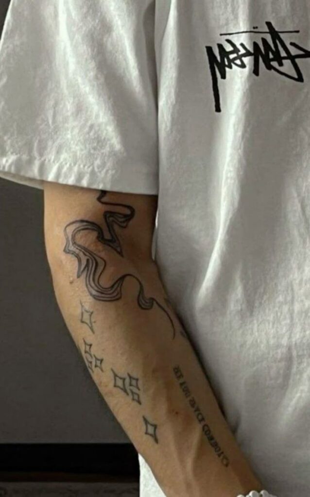 Arm with abstract line and geometric tattoos, wearing a white t-shirt.