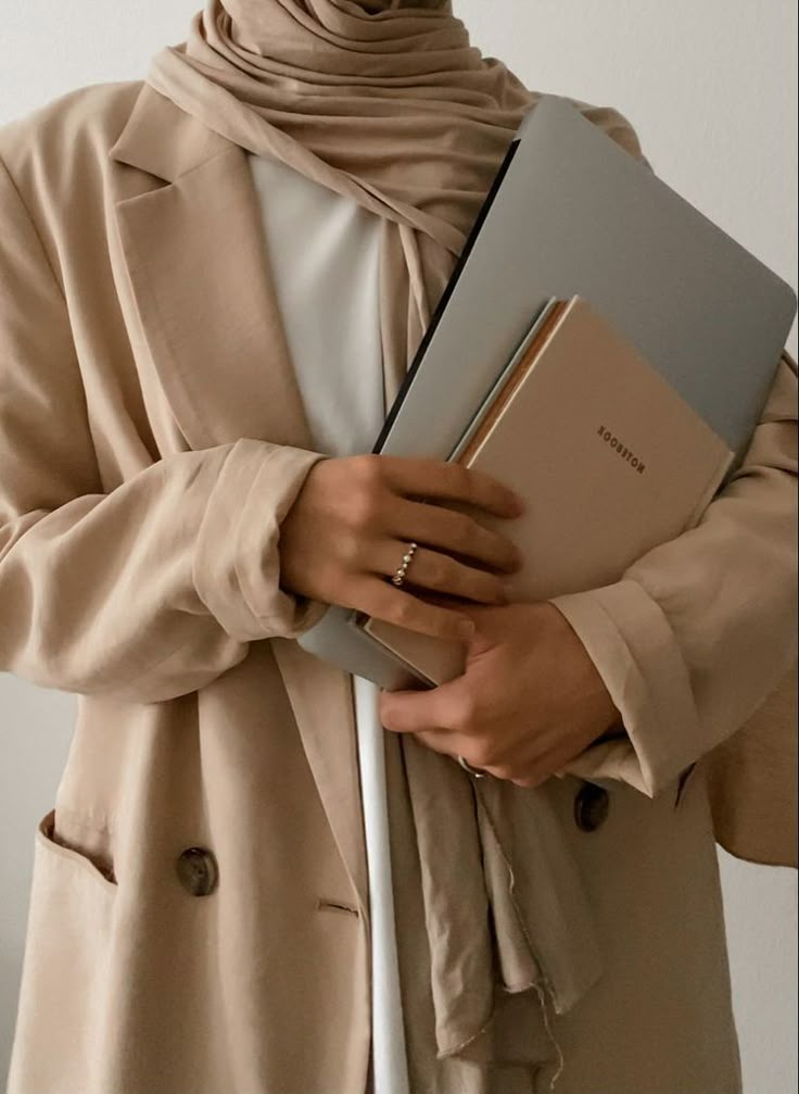 Person in beige coat holding a notebook and tablet, exemplifying professional and stylish attire.