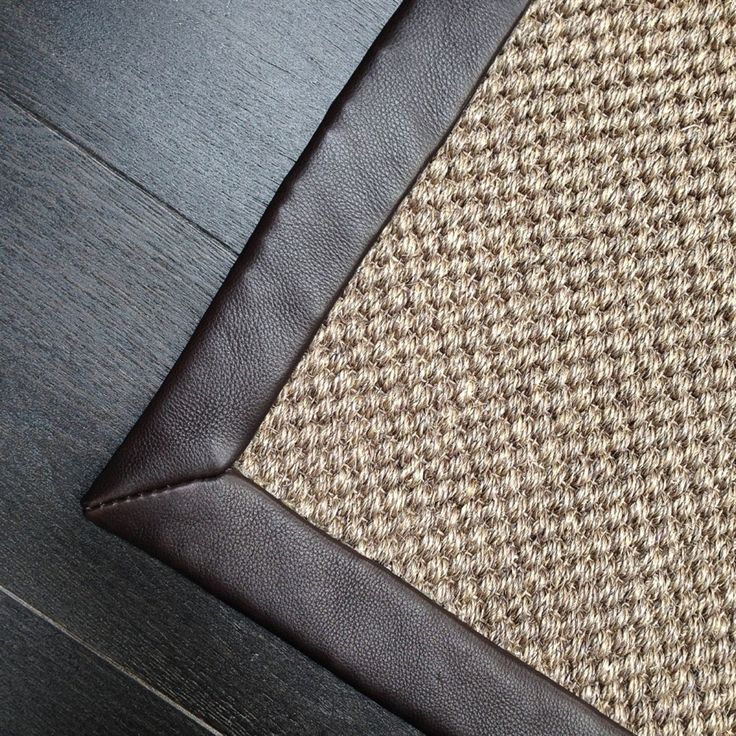 Close-up of a textured rug with a dark leather border on a wooden floor, showcasing modern home interior design.