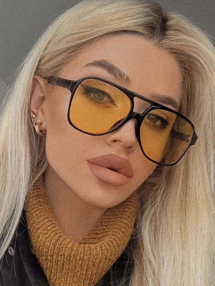 Woman with blonde hair wearing large orange-tinted sunglasses and a mustard turtleneck sweater.