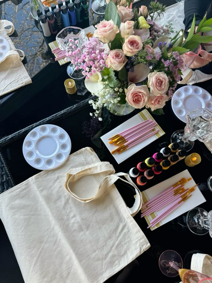 Art supplies and flowers arranged on a table, featuring paint brushes, color palettes, and a canvas bag for painting.