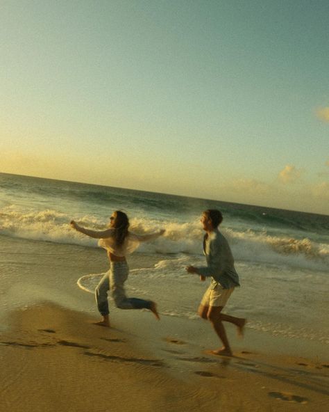 Couple joyfully running on a sandy beach by the ocean under a clear sky.