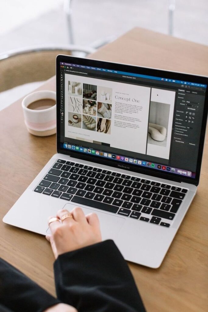 Person working on a MacBook with design software, coffee cup on desk nearby.