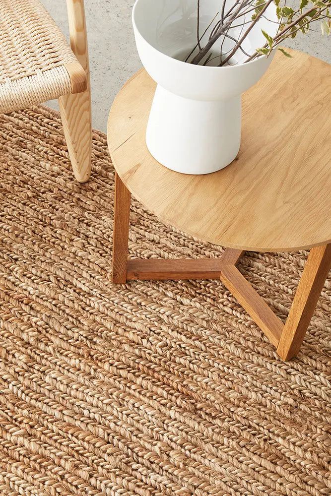 Modern woven rug with wooden chair and table, featuring a white vase with branches for a minimalist home decor.