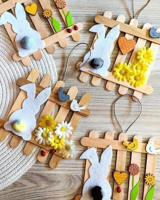 Crafted bunny decorations with popsicle sticks, felt, and colorful flowers on a wooden surface.