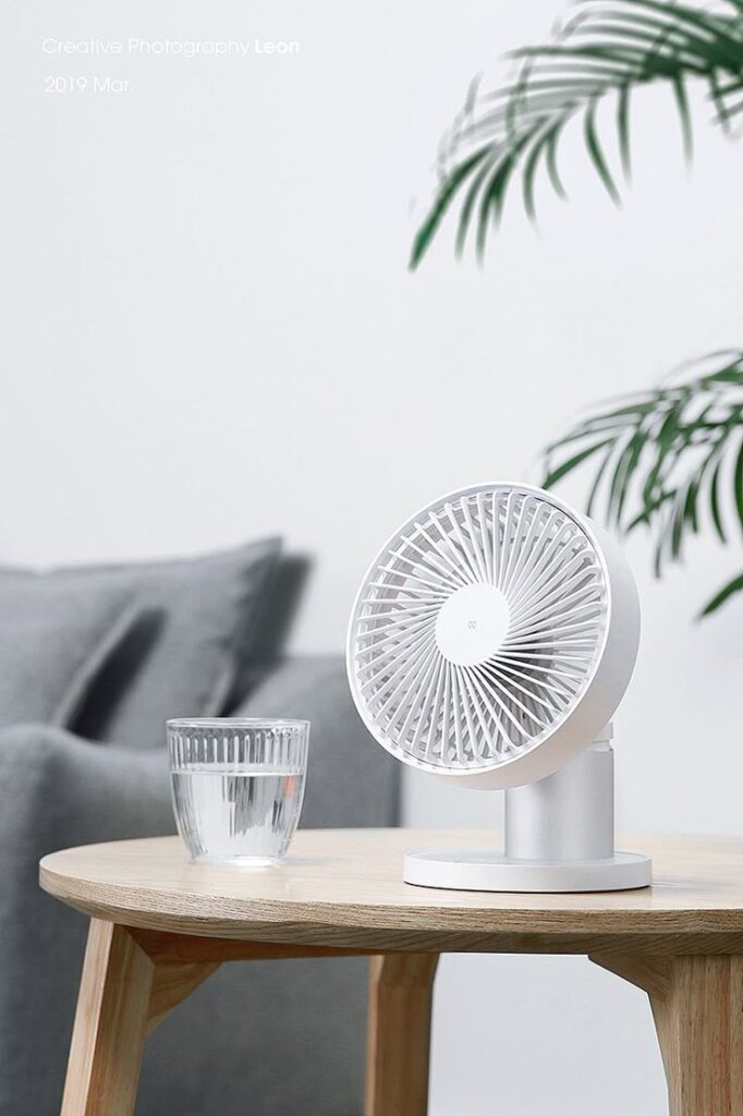 Portable white fan and glass of water on wooden table in minimalist living room with plants.