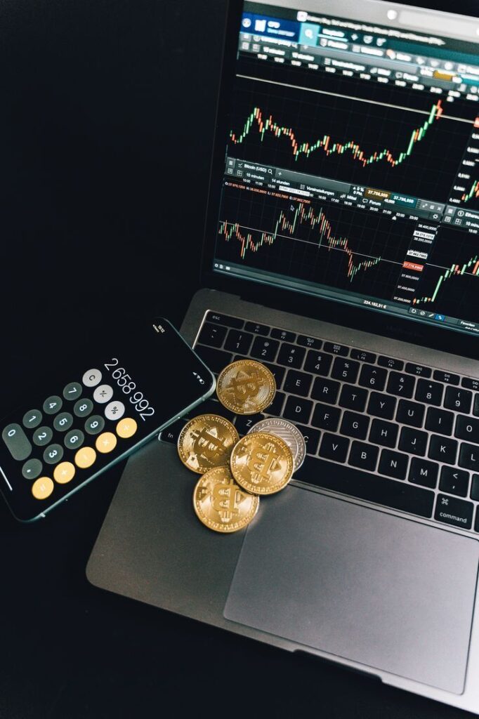 Laptop showing financial charts with Bitcoin coins and calculator on desk.