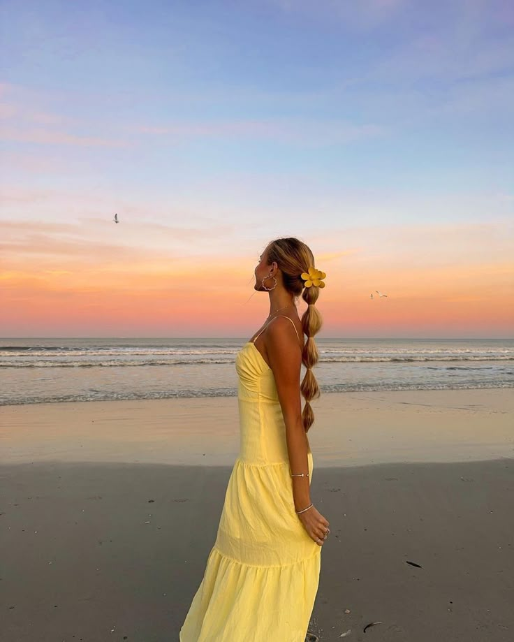 Woman in yellow dress enjoying a colorful sunset at the beach, with gentle waves in the background.