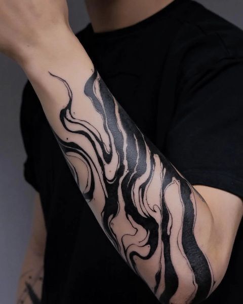 Abstract black ink tattoo design on forearm, showcasing swirling patterns and fluid lines on a person's skin.