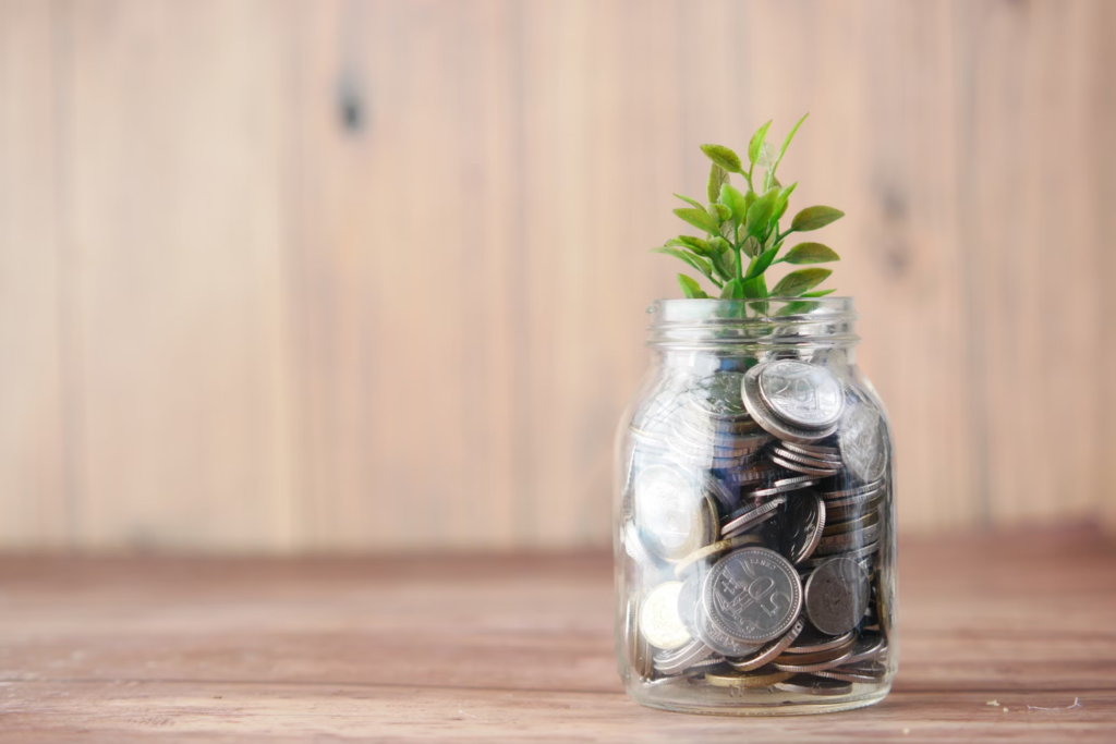 Jar filled with coins and a small plant, symbolizing financial growth and savings on a wooden background.