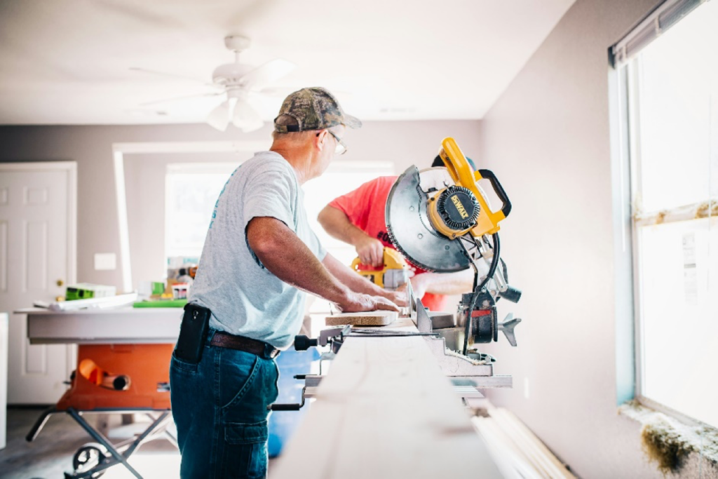 Two men using a miter saw in a bright room for home renovation or woodworking project.