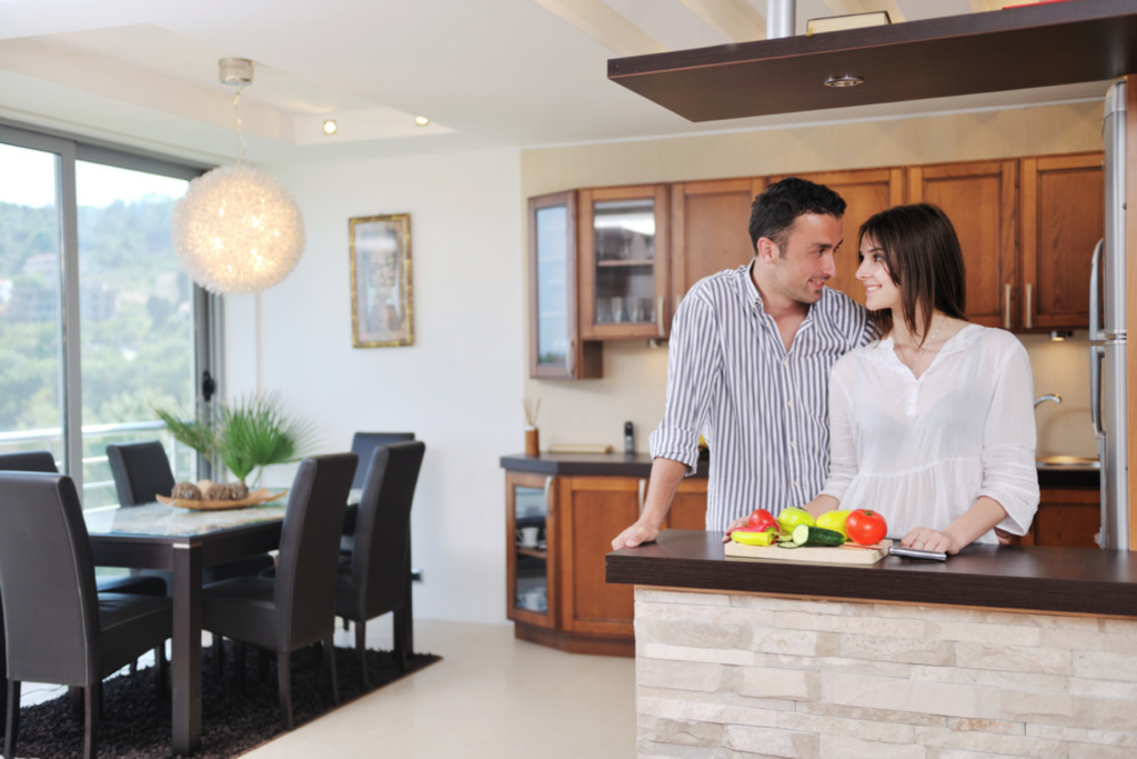 Couple smiling in modern kitchen with fresh vegetables on the counter.