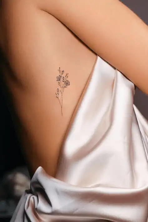 image Delicate floral tattoo on a person's side under silky white fabric, showcasing minimalist body art and elegant tattoo placement. | Sky Rye Design Delicate floral tattoo on a person's side under silky white fabric, showcasing minimalist body art and elegant tattoo placement.