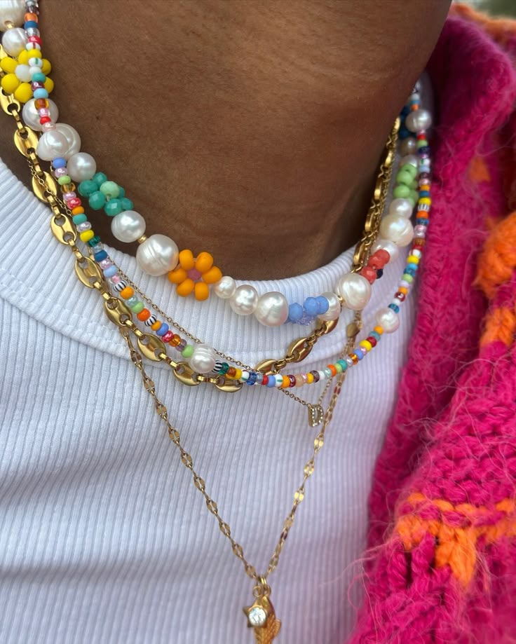 Layered beaded and pearl necklaces on a person wearing a white shirt and vibrant pink and orange knit.