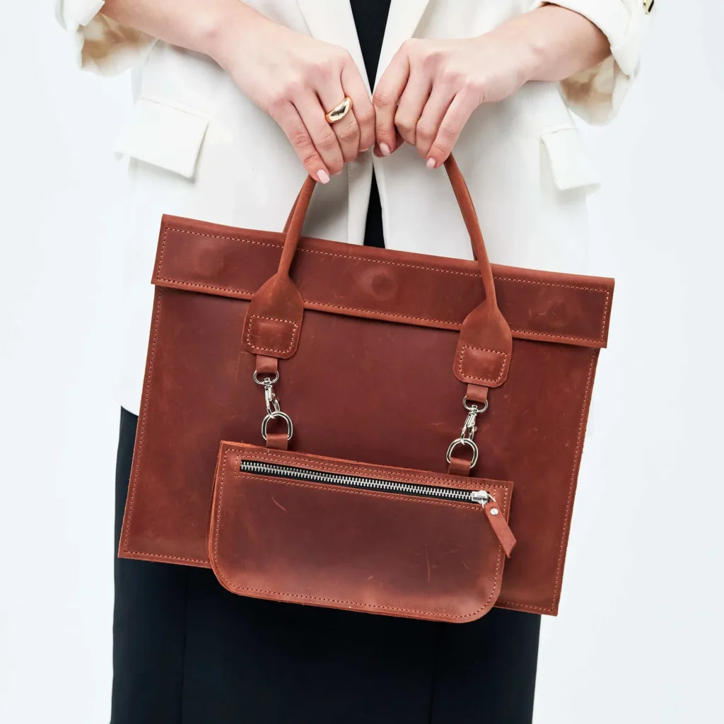 Woman holding a stylish brown leather handbag with detachable pouch, wearing a white blazer.