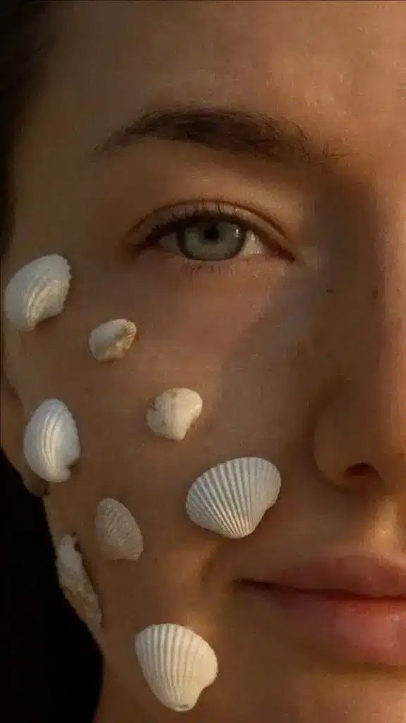 photo girl at sea with shells _ фото идея девушки на море с ракушками Close-up of a woman's face with small seashells artfully arranged on her cheek, highlighting natural beauty. | Sky Rye Design Close-up of a woman's face with small seashells artfully arranged on her cheek, highlighting natural beauty.