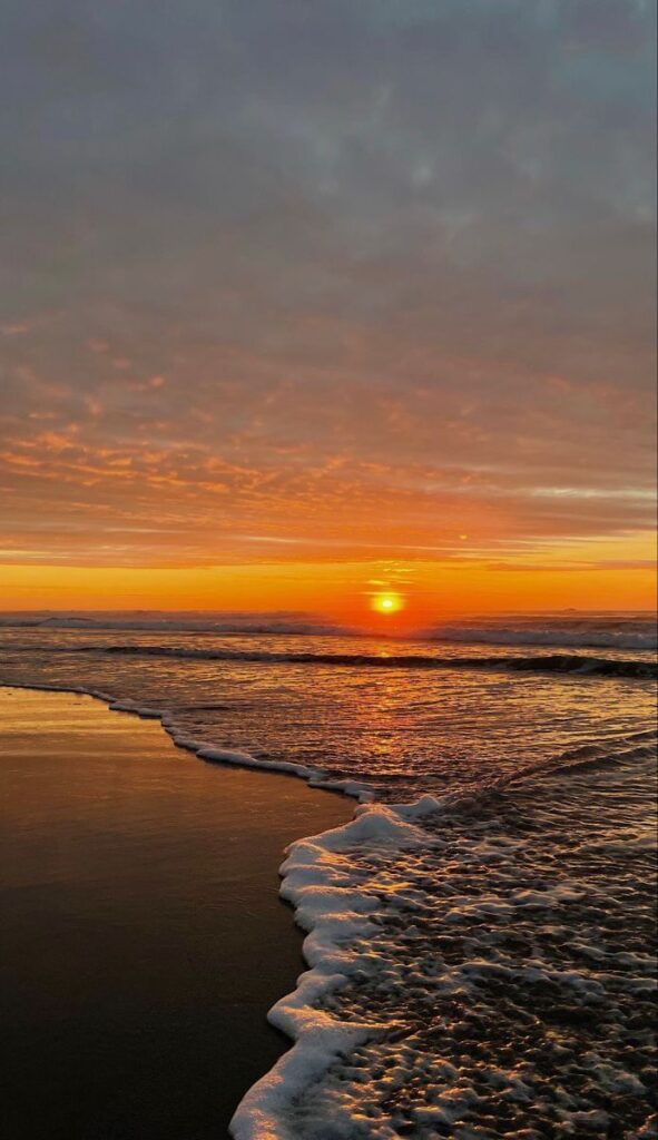 Golden sunset over ocean waves on a sandy beach, with colorful sky and reflections in the water.