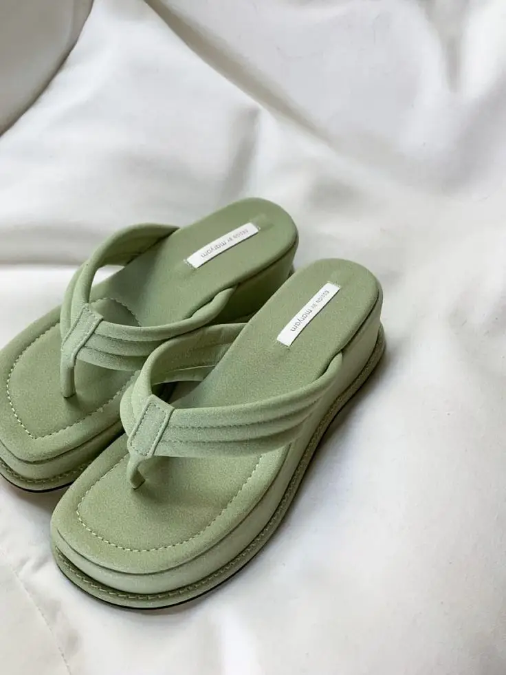 Light green flip-flop wedge sandals on white fabric background, stylish and comfortable summer footwear.