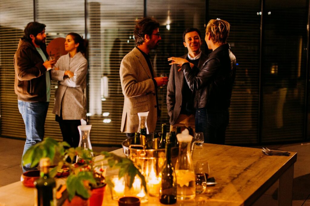 Casual gathering with people chatting over drinks in a warmly lit indoor setting with candles and bottles.