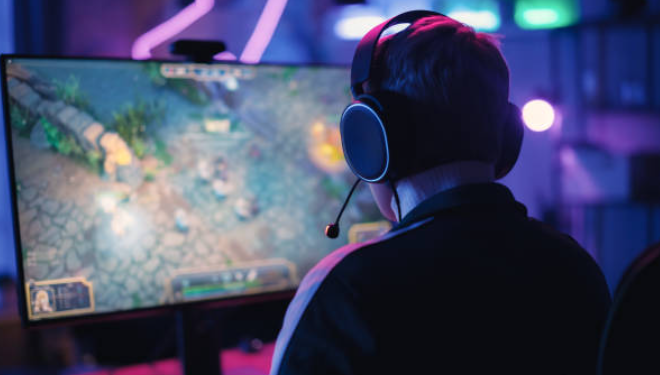 Gamer playing an online strategy game on a PC with headphones in a dimly lit room.