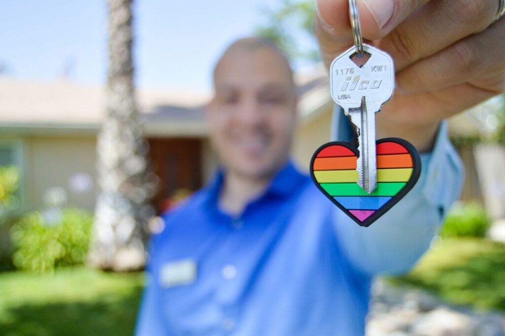 Person holding a key with a rainbow heart keychain, symbolizing LGBT pride and home ownership.