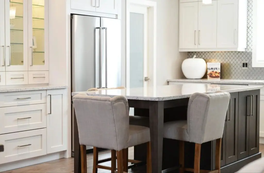Modern kitchen with white cabinets, island seating, and stainless steel fridge. Stylish and elegant design.