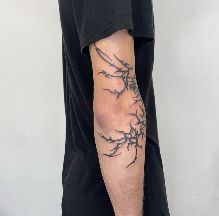 Abstract tribal tattoo on person's arm, featuring bold, jagged lines in black ink on light skin background.