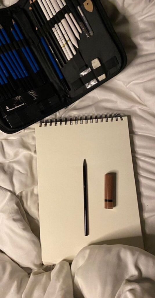 Art sketchbook and pencil set placed on a bed, ideal for drawing inspiration and creativity.