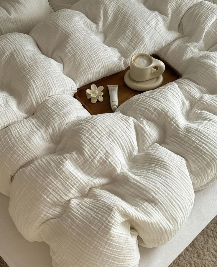 Cozy white bedding with a wooden tray holding coffee, skincare, and a flower accent for a tranquil morning vibe.